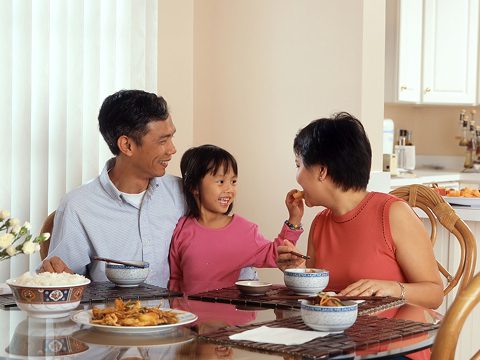 Una familia de tres miembros sentados a la mesa del comedor, comiendo y sonriendo.